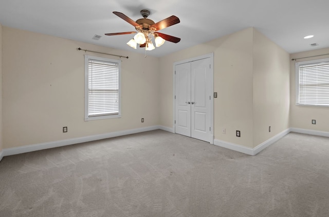 unfurnished bedroom with a closet, multiple windows, light colored carpet, and ceiling fan