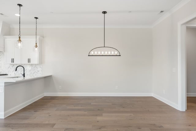 unfurnished dining area featuring sink, light hardwood / wood-style flooring, and crown molding