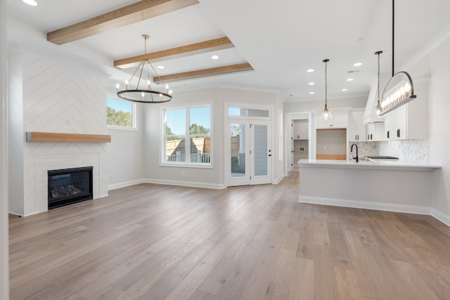 unfurnished living room with a large fireplace, crown molding, beamed ceiling, and light hardwood / wood-style flooring