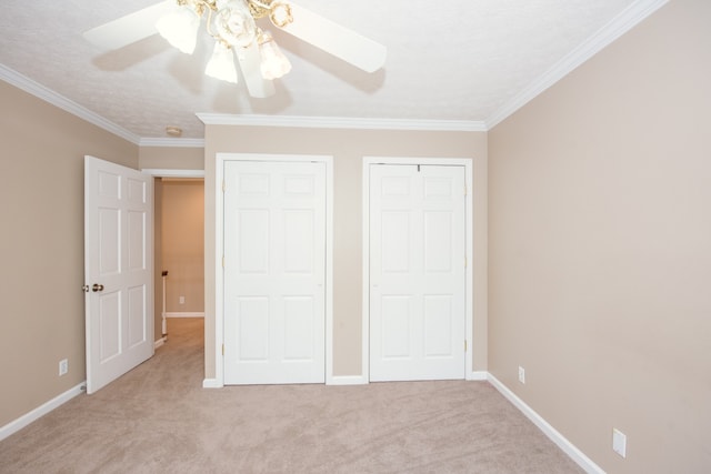 unfurnished bedroom with ceiling fan, light carpet, ornamental molding, and two closets