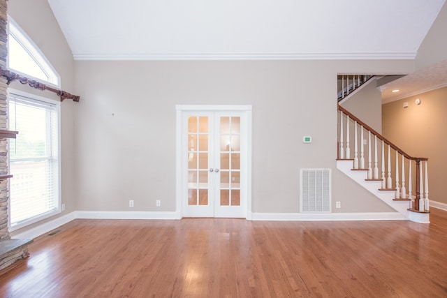 unfurnished living room with lofted ceiling, hardwood / wood-style flooring, ornamental molding, a stone fireplace, and french doors