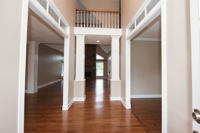 entryway featuring crown molding, decorative columns, a fireplace, and dark hardwood / wood-style flooring