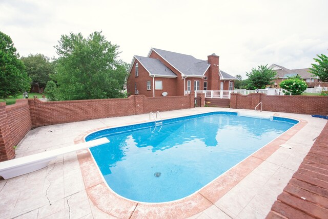 view of swimming pool featuring a diving board and a patio