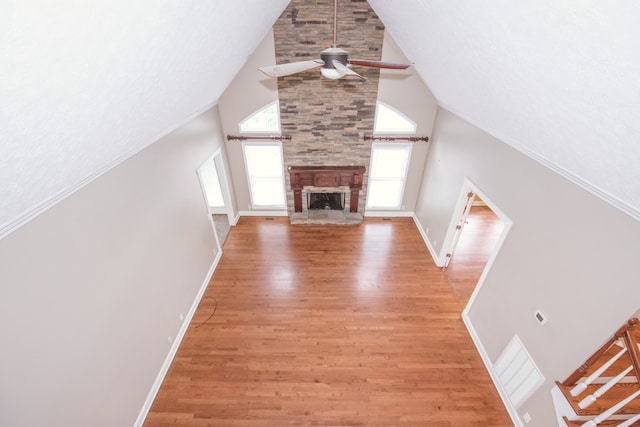 unfurnished living room featuring high vaulted ceiling, a stone fireplace, wood-type flooring, and ceiling fan