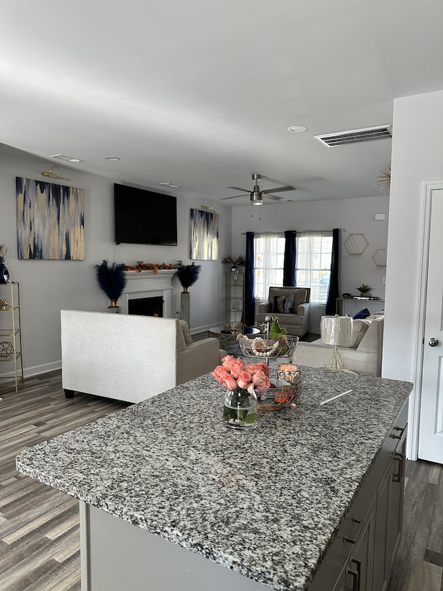 kitchen featuring dark wood-type flooring, a center island, gray cabinets, light stone counters, and ceiling fan