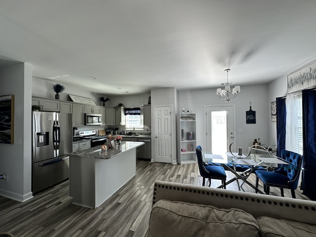 kitchen with dark hardwood / wood-style flooring, appliances with stainless steel finishes, a kitchen island, gray cabinetry, and decorative light fixtures