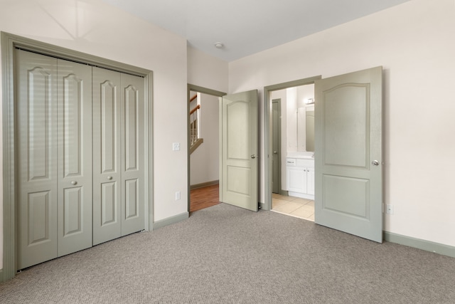 unfurnished bedroom featuring light carpet, a closet, and ensuite bath