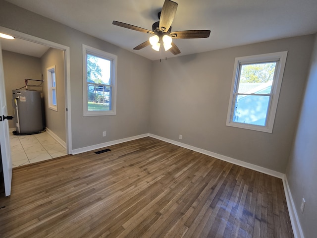 spare room featuring ceiling fan, plenty of natural light, light hardwood / wood-style floors, and water heater