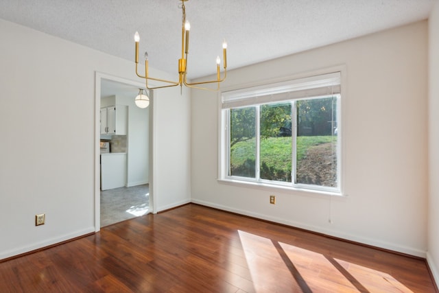 unfurnished dining area with hardwood / wood-style floors, a textured ceiling, and an inviting chandelier