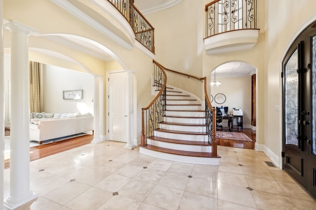 entryway with crown molding, decorative columns, tile patterned floors, and a high ceiling