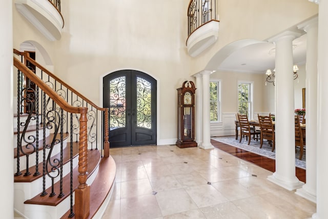 tiled entryway with crown molding, decorative columns, french doors, and a towering ceiling