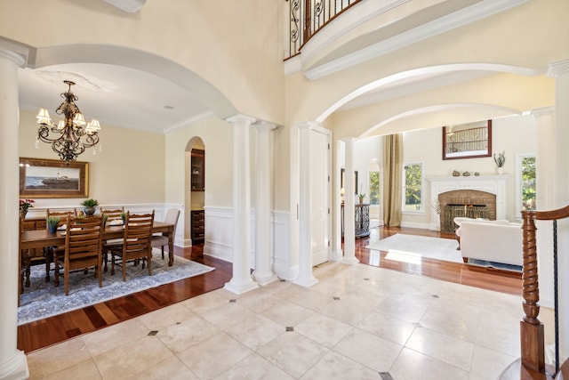 foyer featuring crown molding, light tile patterned floors, a fireplace, decorative columns, and a high ceiling