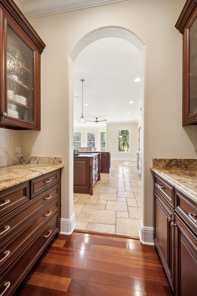 kitchen featuring light stone counters, crown molding, dark brown cabinets, hanging light fixtures, and light hardwood / wood-style floors