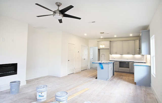 kitchen featuring gray cabinetry, sink, light hardwood / wood-style floors, decorative light fixtures, and a kitchen island with sink