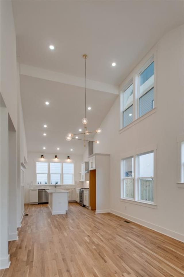 unfurnished living room featuring light hardwood / wood-style flooring, a chandelier, high vaulted ceiling, and a wealth of natural light