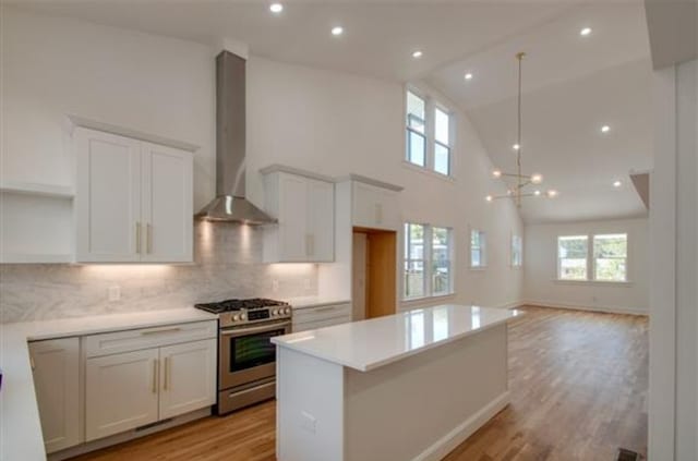 kitchen with stainless steel gas range, backsplash, wall chimney range hood, and light hardwood / wood-style floors