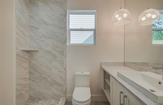 bathroom featuring a healthy amount of sunlight, vanity, tiled shower, and toilet