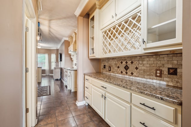 kitchen with tasteful backsplash, a textured ceiling, light stone countertops, ornamental molding, and dark tile patterned flooring