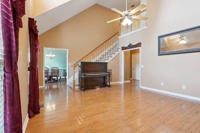 unfurnished living room featuring high vaulted ceiling, light wood-type flooring, and ceiling fan with notable chandelier