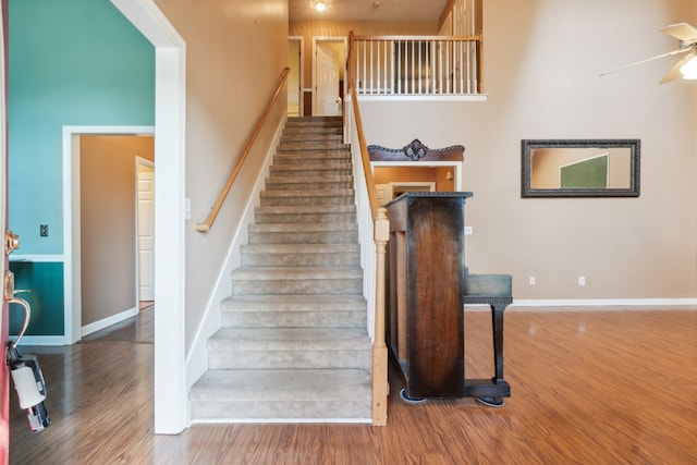 stairs featuring a towering ceiling, hardwood / wood-style floors, and ceiling fan