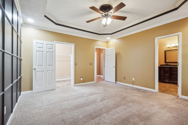 unfurnished bedroom with a spacious closet, ceiling fan, crown molding, and a raised ceiling