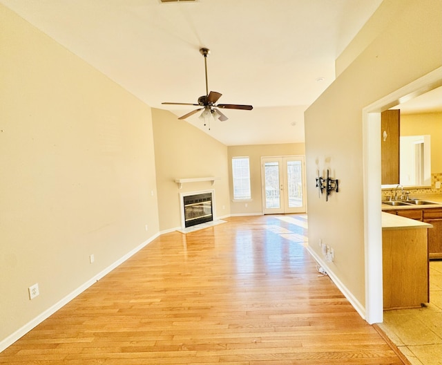 unfurnished living room featuring french doors, lofted ceiling, sink, ceiling fan, and light hardwood / wood-style floors