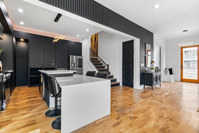 kitchen with light hardwood / wood-style flooring, a kitchen island with sink, hanging light fixtures, and stainless steel appliances