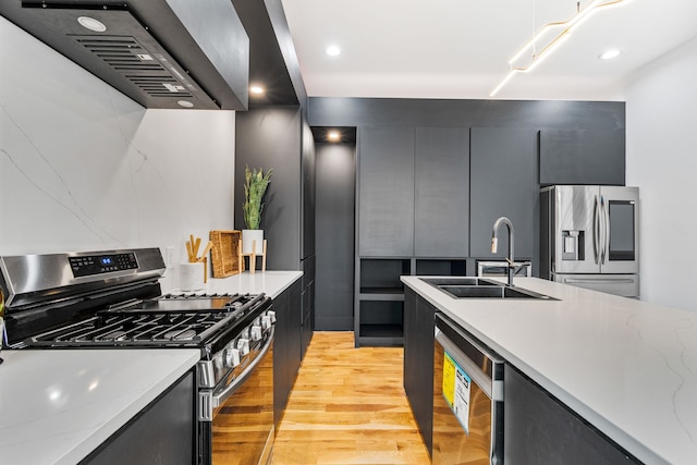 kitchen featuring exhaust hood, light stone counters, appliances with stainless steel finishes, light wood-type flooring, and sink