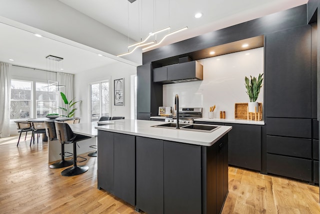 kitchen with light hardwood / wood-style floors, decorative light fixtures, sink, and an island with sink