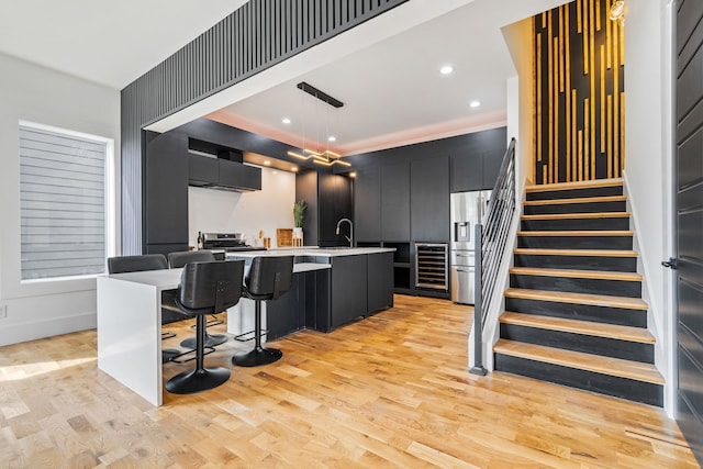 kitchen featuring a kitchen breakfast bar, a kitchen island with sink, light wood-type flooring, stainless steel appliances, and decorative light fixtures