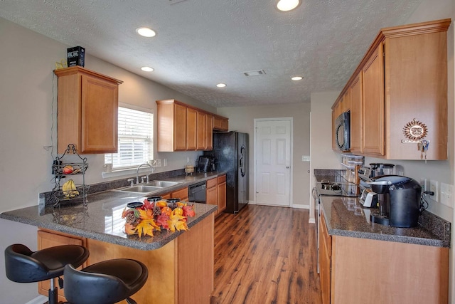 kitchen with kitchen peninsula, a textured ceiling, hardwood / wood-style flooring, black appliances, and sink