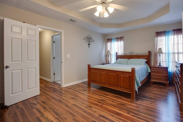 bedroom featuring multiple windows, dark hardwood / wood-style floors, a raised ceiling, and ceiling fan