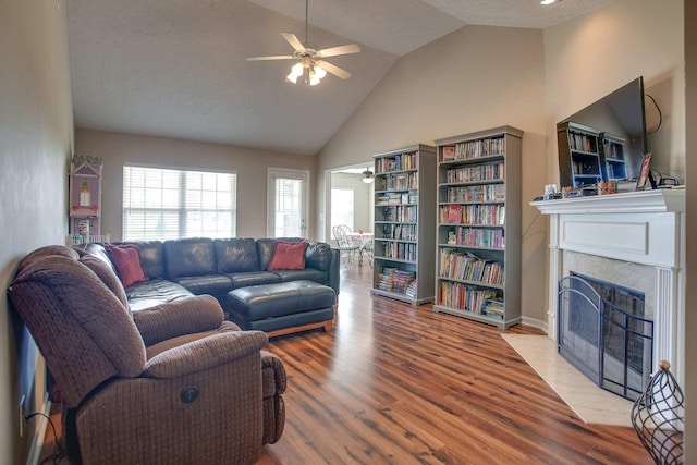 living room with a textured ceiling, hardwood / wood-style flooring, a tiled fireplace, and ceiling fan