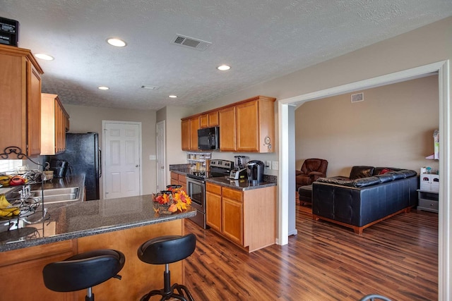 kitchen with kitchen peninsula, a textured ceiling, stainless steel appliances, and dark wood-type flooring