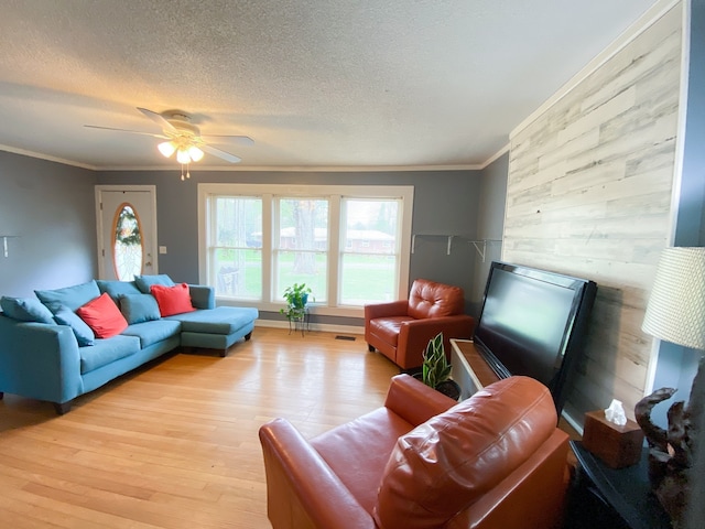 living room with light hardwood / wood-style floors, a textured ceiling, wooden walls, ceiling fan, and crown molding