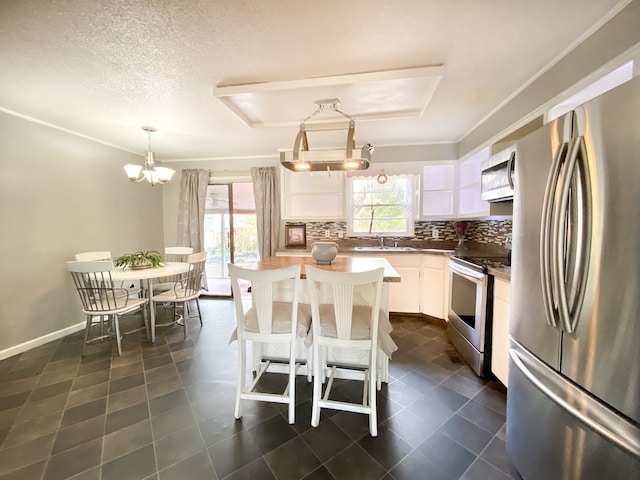 kitchen featuring stainless steel appliances, white cabinets, decorative backsplash, a notable chandelier, and pendant lighting