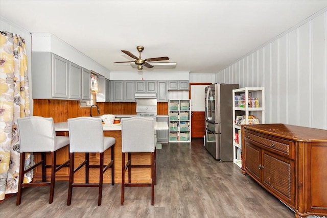 kitchen with a kitchen bar, ceiling fan, gray cabinets, dark hardwood / wood-style flooring, and stainless steel refrigerator