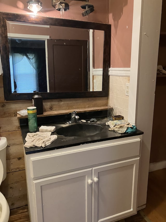 bathroom with vanity, toilet, and wood walls