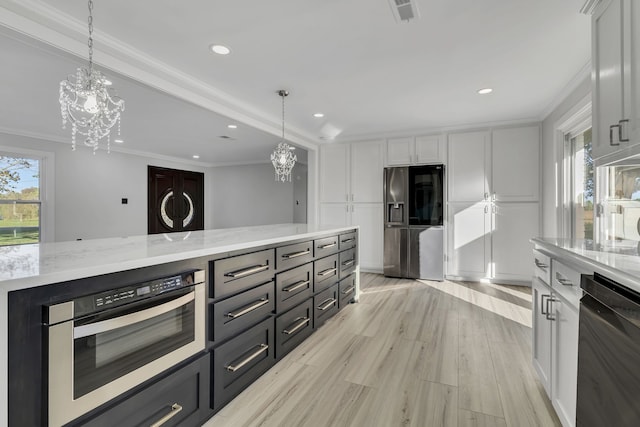 kitchen with appliances with stainless steel finishes, pendant lighting, white cabinets, ornamental molding, and light hardwood / wood-style flooring