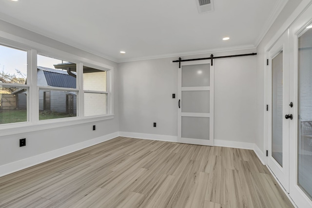 spare room featuring ornamental molding, light hardwood / wood-style flooring, and a barn door