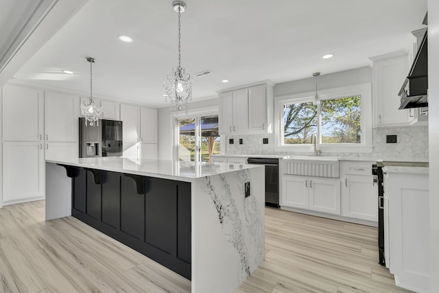 kitchen featuring dishwasher, light wood-type flooring, a spacious island, black fridge, and white cabinets