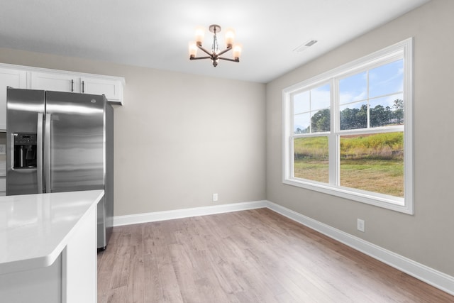 kitchen with white cabinetry, stainless steel fridge, an inviting chandelier, and light wood-type flooring