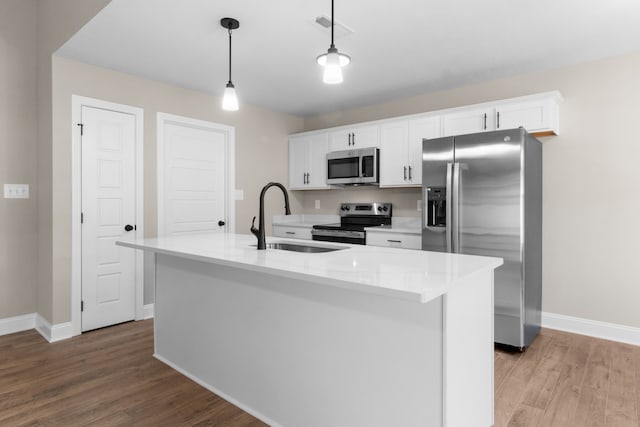 kitchen with appliances with stainless steel finishes, pendant lighting, sink, white cabinets, and a kitchen island with sink