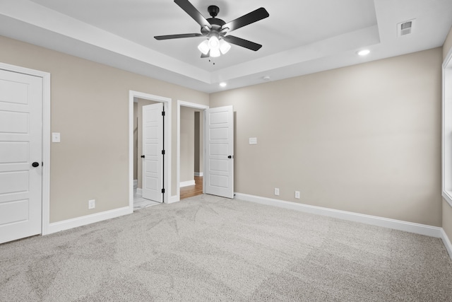 unfurnished bedroom featuring light carpet, a tray ceiling, and ceiling fan