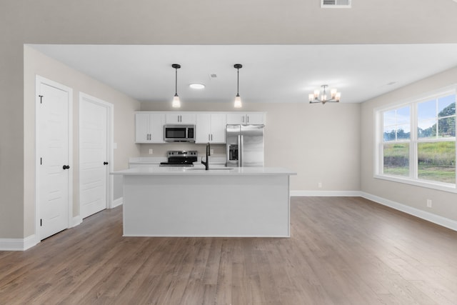 kitchen with sink, white cabinets, hanging light fixtures, stainless steel appliances, and a center island with sink