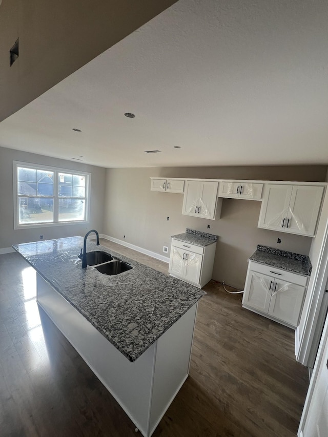 kitchen with sink, white cabinetry, dark stone countertops, dark hardwood / wood-style flooring, and an island with sink