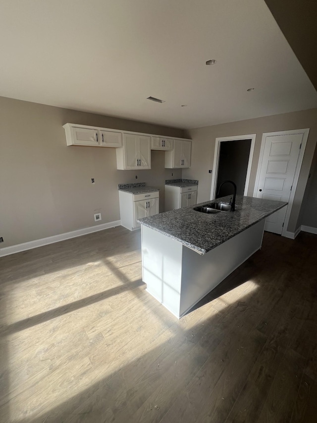 kitchen with sink, light hardwood / wood-style flooring, stone counters, white cabinetry, and a center island with sink