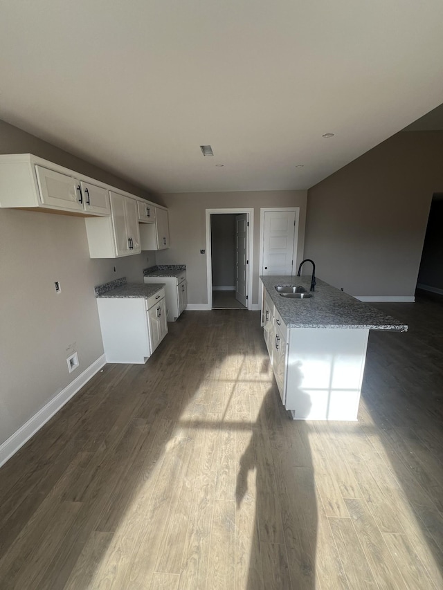 kitchen featuring sink, stone counters, wood-type flooring, an island with sink, and white cabinets