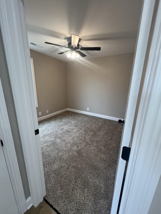 unfurnished room with visible vents, baseboards, dark colored carpet, and a ceiling fan