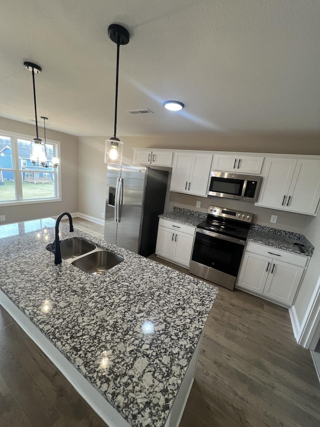 kitchen with dark wood finished floors, appliances with stainless steel finishes, white cabinetry, a sink, and dark stone counters